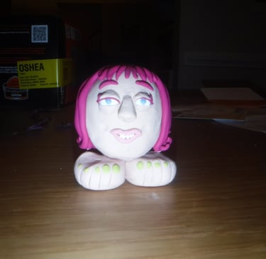 Handmade clay figurine of a pink-haired face resting on white feet with green toes.