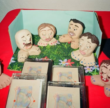 Handmade clay figurines of cartoon faces on feet displayed with cassette tapes on a red surface.