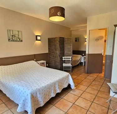 Chambre chocolat avec un grand li et un petit lit séparé d'un paravent avec salle de bain.