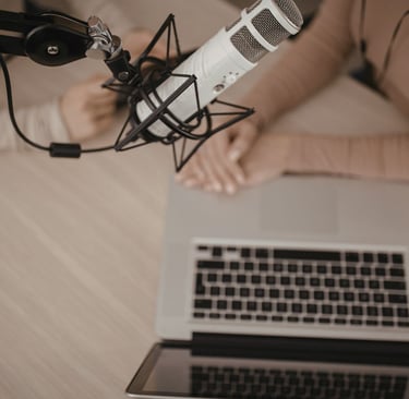 Professional condenser microphone in a podcast studio with two hosts using a laptop for recording.