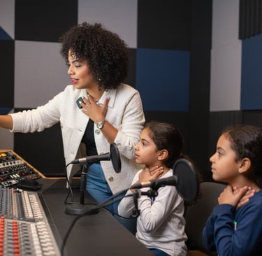 A music teacher and students use a professional audio mixing board in a recording studio.