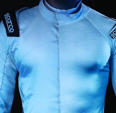 A driver wearing a white Sparco fireproof racing suit with visible shoulder patches and safety padding.