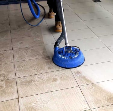 Professional floor cleaner using a rotary pressure tool to deep clean dirty ceramic tile and grout.