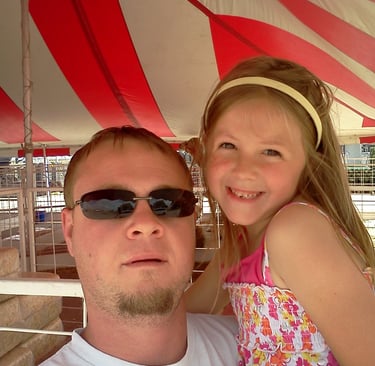 Man wearing dark sunglasses and child are posing under a red and white striped canopy