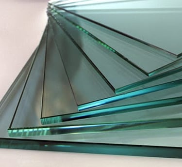 Stack of thick tempered glass sheets with polished edges and blue tint for industrial construction.