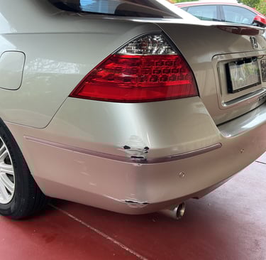 Rear bumper damage with paint scuffs and scratches on a silver sedan parked on a red driveway.