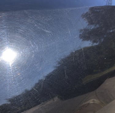 Close-up of swirl marks and light scratches on black car paint needing paint correction..