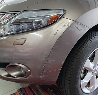 Close-up of a scratched silver car bumper and fender before Lev Auto Refinishing.