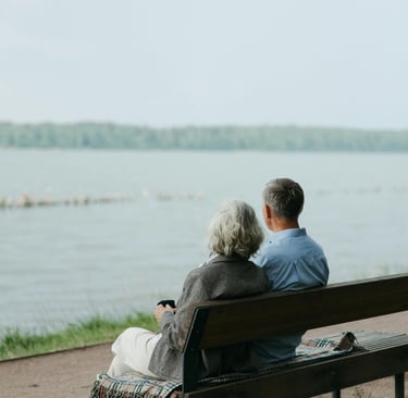 a man and woman sitting on a bench in front of a lake