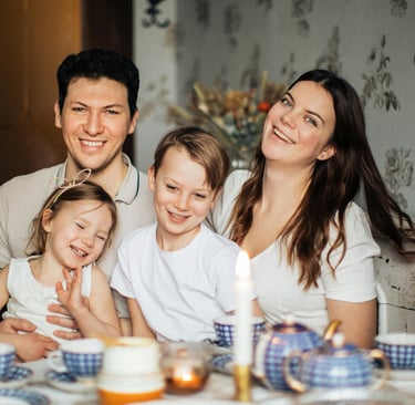 A happy family of four smiling together during a cozy tea time at home with vintage blue tea sets.