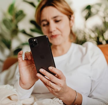 A woman relaxing on a leather sofa uses her smartphone with indoor plants in the background.