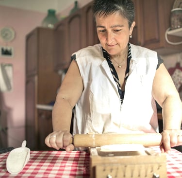 A woman using a wooden rolling pin to make fresh homemade pasta in a rustic kitchen.