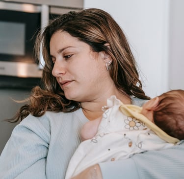 A mother holding her newborn baby at home in a kitchen setting, focusing on postpartum care.