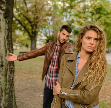 A young couple in a park having a relationship argument as the woman looks away frustrated.
