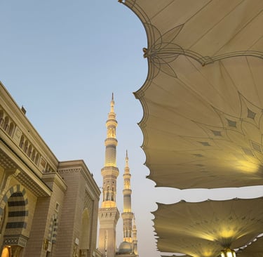 Illuminated minarets of Al-Masjid an-Nabawi in Medina beneath large white umbrellas at dusk.