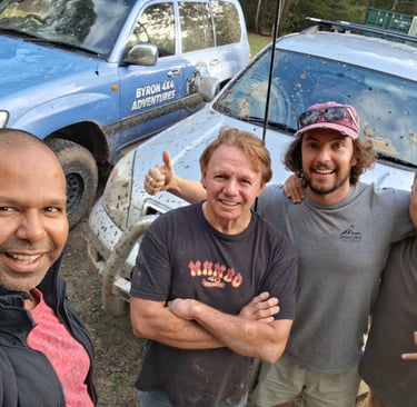 A group of four men posing for a selfie after a Byron 4x4 adventures off-roading trip with muddy SUVs.