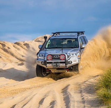 Silver Toyota Land Cruiser 200 Series off-roading through sand dunes with ARB bull bar and accessories.