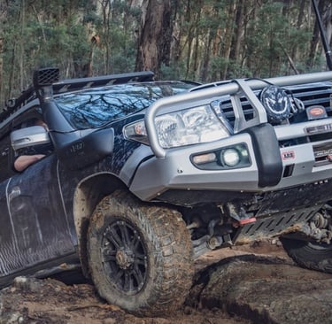 Toyota Land Cruiser 200 series 4WD with bull bar and snorkel driving over rocky terrain.