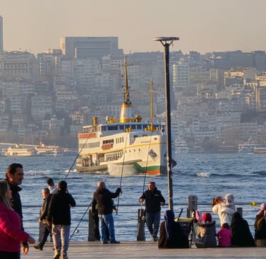 People fishing on a pier with a large ferry boat sailing across the Bosphorus in Istanbul.