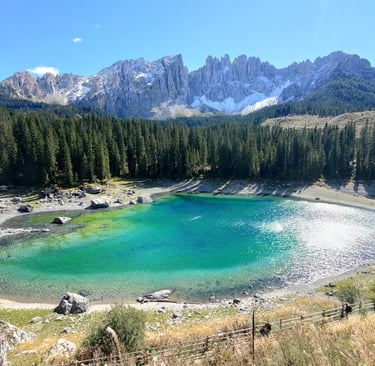Panoramic view of the emerald green Lake Carezza in the Dolomites, surrounded by pine forests and jagged mountains.