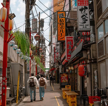Crowded narrow alley in Tokyo's Shinjuku district featuring colorful restaurant signs and traditional lanterns.