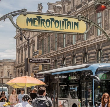 Classic Art Nouveau Metropolitain subway sign above a busy Paris street with a blue electric bus and pedestrians.