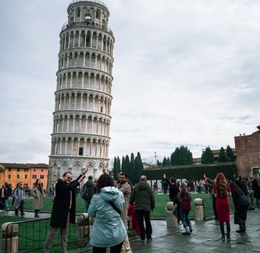 Tourists posing for photos in front of the Leaning Tower of Pisa in Italy on a cloudy day.
