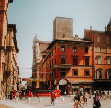 Crowded public square in Bologna, Italy, with red brick buildings and a medieval stone tower.