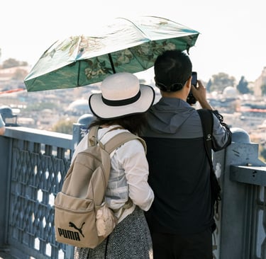 A couple with a sun umbrella and backpack sightseeing and taking photos from a bridge in Istanbul.