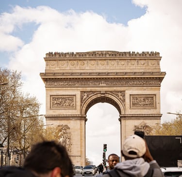 Tourists taking photos of the Arc de Triomphe monument in Paris under a blue sky.
