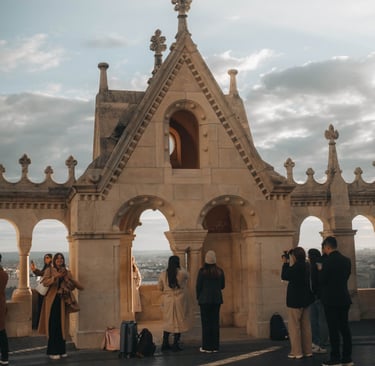 Tourists taking photos at the Fisherman's Bastion stone lookout in Budapest, Hungary at sunset.