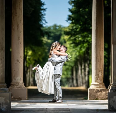 Bräutigam hebt seine Braut lachend in die Höhe – romantischer Hochzeitsmoment in Mailand unter alten Säulen.