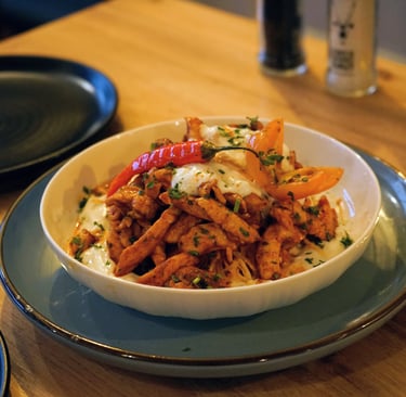 Spicy chicken strips served over creamy yogurt sauce with red peppers and fresh herbs in a white bowl.