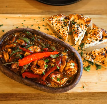 Spicy shrimp stew served in a traditional clay pot with sliced sesame bread on a wooden board.