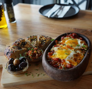 Authentic shakshuka with baked eggs in a stone bowl served with pita bread and olives on a wooden board.