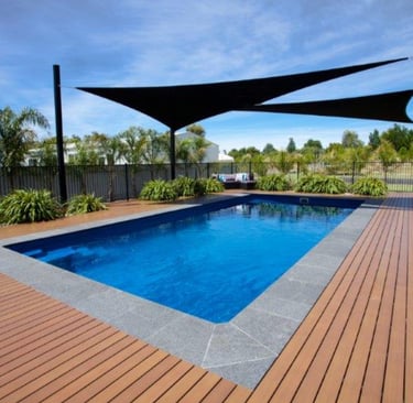 Modern rectangular pool with timber decking, deep blue water and grey stone coping tiles.