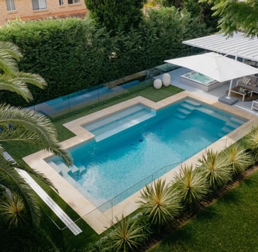 Geometric Rectangular pool with soft aqua water and beige coping tiles framed by lush green hedges