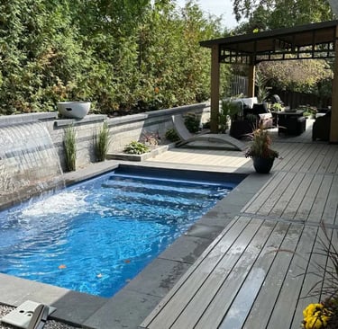 Modern lap pool with deep blue water and dark grey stone tiles, featuring a sleek waterfall wall