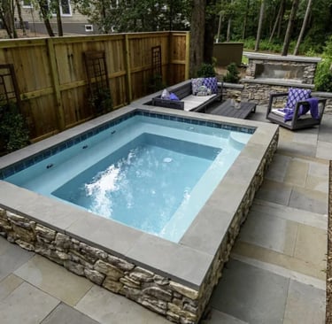 Raised square spa pool with pale blue water and grey stone coping and tiles in a modern garden setti