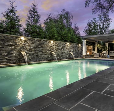 Modern rectangular lap pool with soft green water, dark stone wall and charcoal grey tiled surrounds