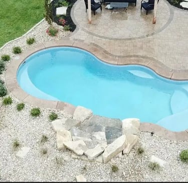 Freeform pool with attached spa, deep teal water and warm beige mosaic tile interior.