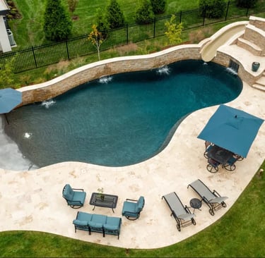 Freeform curved pool with deep teal water and dark mosaic tiles, edged with natural stone terraces