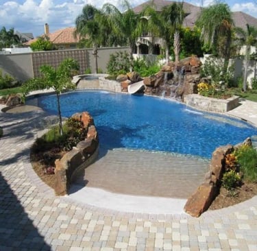 Natural lagoon pool with blue water, rock features and sandy-toned paving with subtle mosaic tiling