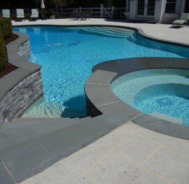 Curved pool and spa combo with light blue water, grey coping and matching grey interior tiles