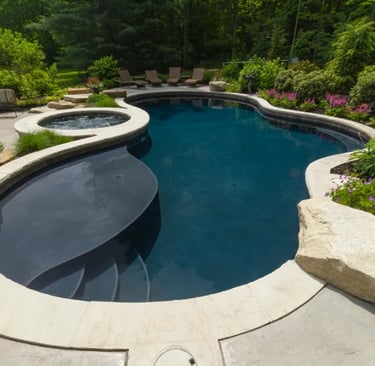 Freeform lagoon pool with dark blue water, smooth curves and light stone coping with dark interior t