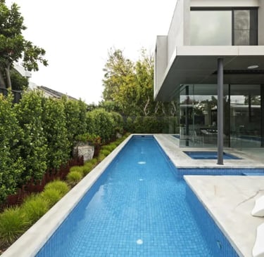 Narrow modern lap pool, clear blue water with fine light-blue mosaic tiling and concrete coping.