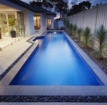 Rectangular backyard lap pool, deep blue water with dark blue mosaic tiles and stone coping.