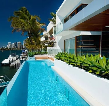 Luxury waterfront lap pool, bright turquoise water with pale blue mosaic tiling and glass edge.