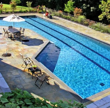 Long rectangular lap pool, clear blue water, pale stone coping with dark lane tile accents