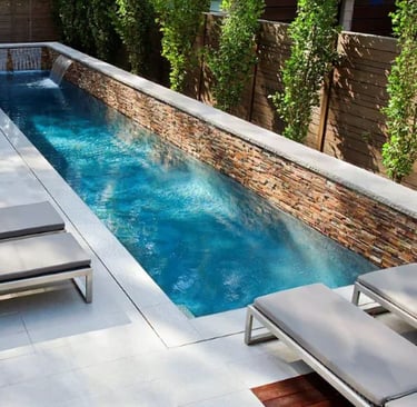 Narrow lap pool with deep blue water, stacked stone feature wall and neutral tile lining.